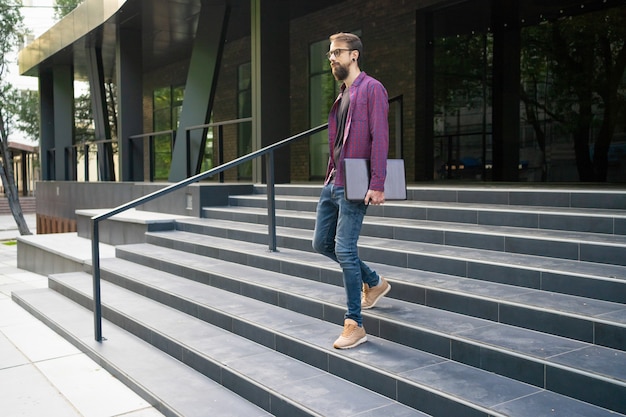 Free photo dark-haired man going down stairs and holding laptop