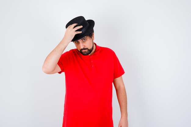 Free photo dark-haired man in red t-shirt adjusting hat , front view.