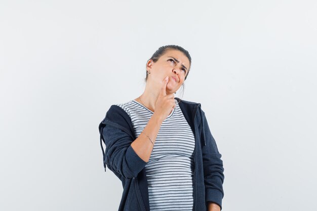 Dark-haired woman holding finger on her jaw in shirt