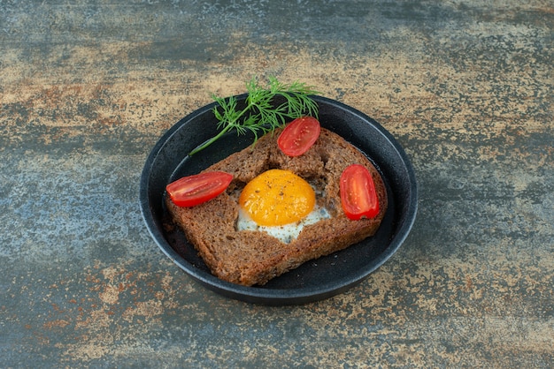 Free photo a dark pan with fried egg and tomato on marble background