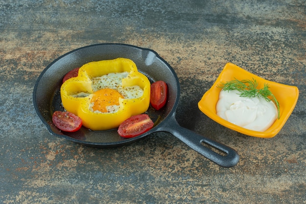 Free photo a dark pan with fried egg and tomato and sour cream on marble background