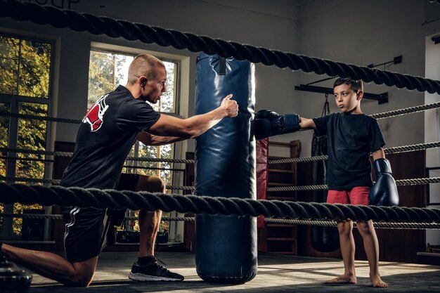 Dark photo shoot of kids training with big punching bag at boxing studio.