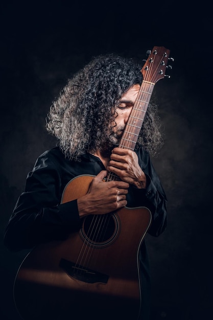 Free photo in dark photo studio curly middle aged man is posing with guitar for photographer.