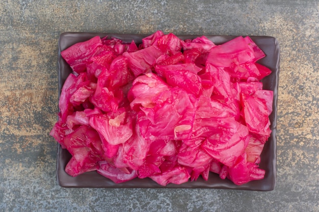 A dark plate full of red salty cabbage on marble background. High quality photo