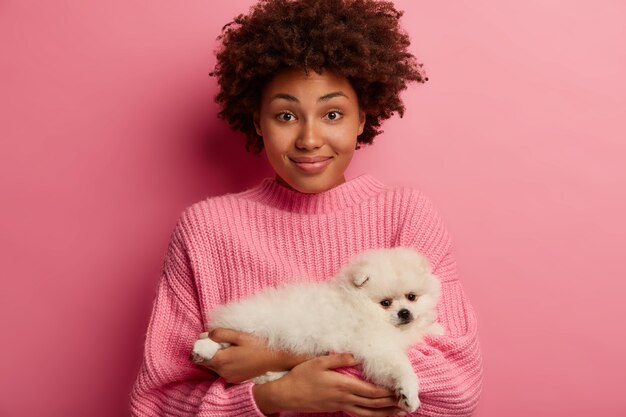 dark skinned lady keeps lips rounded, wants to kiss adorable pet, plays with small puppy