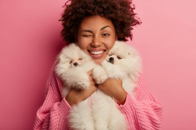 dark skinned lady keeps lips rounded, wants to kiss adorable pet, plays with small puppy