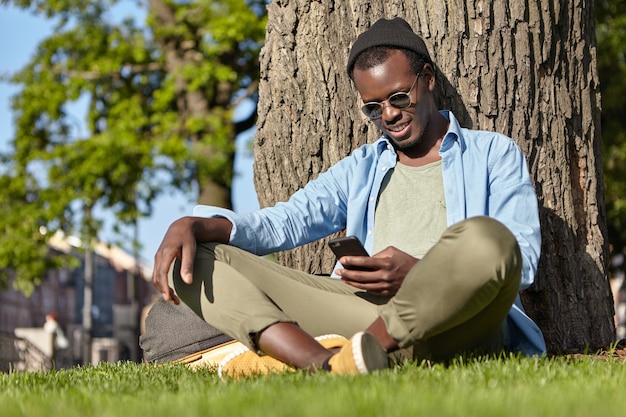 Dark-skinned male sitting on grass near tree