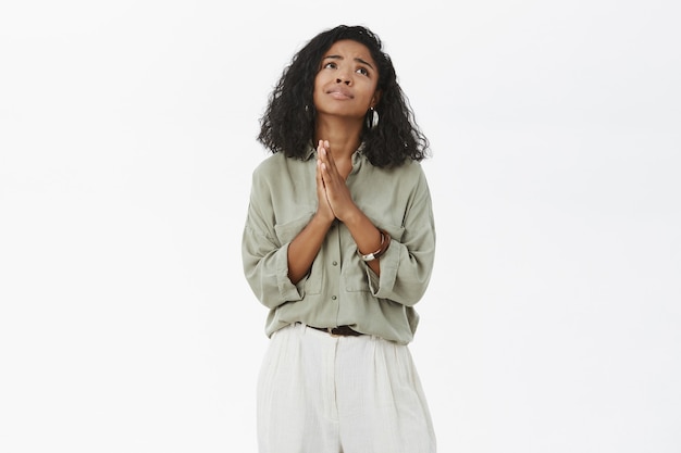 Dark skinned woman holding hands in pray looking up with sad faithful look making wish