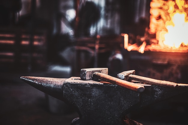 Dark stithy workshop with hammer on anvil at firs plan and fire in stove at background.