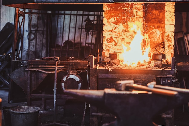 Dark stithy workshop with hammer on anvil at firs plan and fire in stove at background.