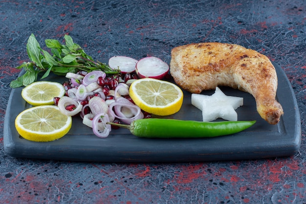 Free photo a dark wooden board of vegetables and chiken leg meat