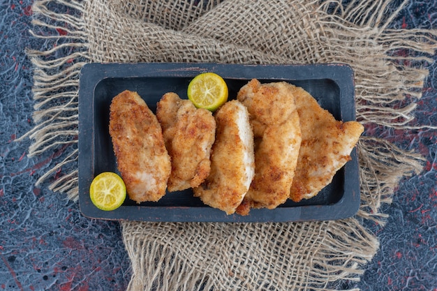 Free photo a dark wooden board with baked chicken meat with slices of lemon .