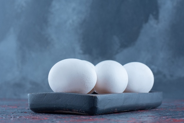 Free photo a dark wooden board with raw white chicken eggs