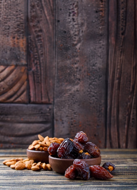 Dates and almonds in clay plates on wooden and stone tile background. side view.