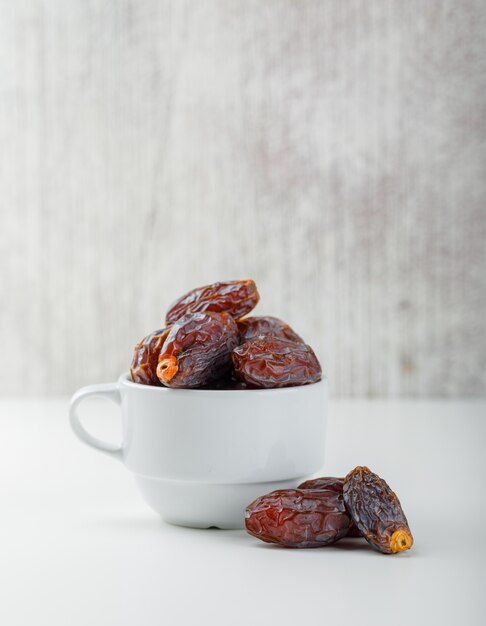 Dates in a white cup on grunge and white table. side view.