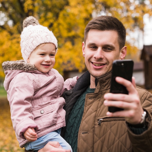 Free photo daughter and father making selfie in autumn park