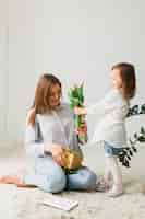 Free photo daughter giving flowers to mother with gift box