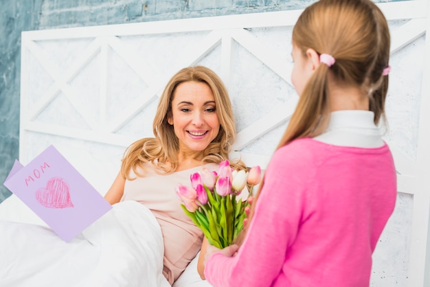 Free photo daughter giving tulips to mother in bed