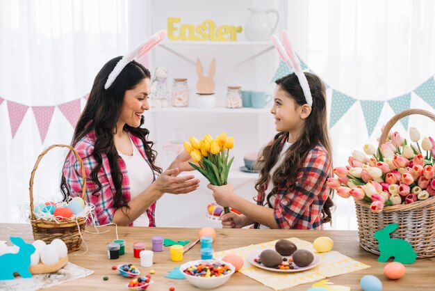 Daughter giving yellow flower tulips to her mother with easter day preparation at home