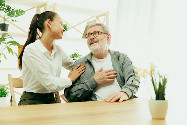 Free photo a daughter or granddaughter spends time with the grandfather or senior man. family or fathers' day, positive emotions and happieness. lifestyle portrait at home. girl taking care about dad.