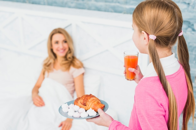 Daughter holding croissant and juice for mother 