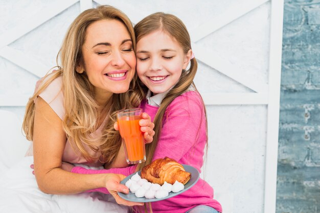 Daughter hugging mother with breakfast on bed 