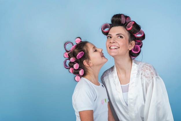 Daughter kissing mother in curlers and bathrobe 