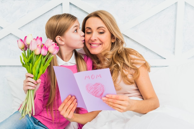 Free photo daughter kissing mother with greeting card