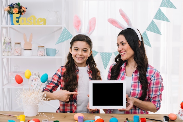 Free photo daughter pointing finger to the digital tablet hold by her mother on easter day