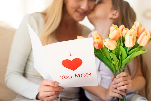 Daughter surprising mother with bouquet of flowers and card