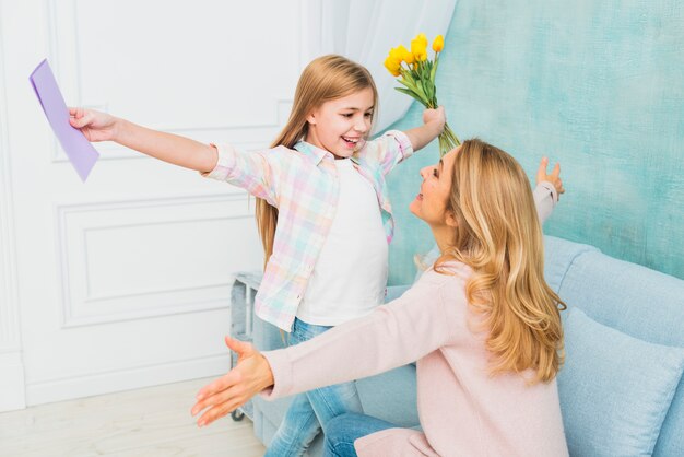 Daughter with gifts flower and postcard hugging mother