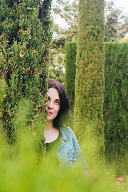 Free photo day dreaming young woman peeking through hedge