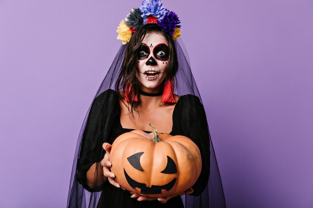 Dead bride with pumpkin in hands expressing amazement. Shocked lady in halloween costume  with mouth open.