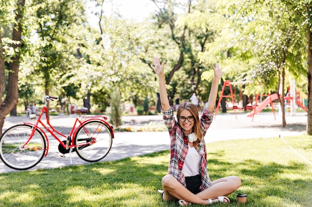 Free photo debonair female model enjoying good spring day in park. enthusiastic girl with wavy hair sitting on green grass.