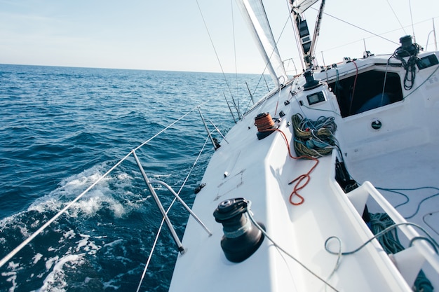 Deck of professional sailboat or racing yacht during competition on sunny and windy summer day, moving fast through waves and water, with spinnaker up