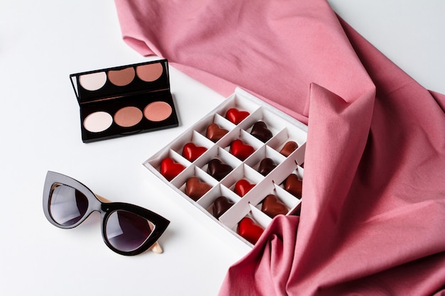 Decorative cosmetics sunglasses and chocolate over white surface