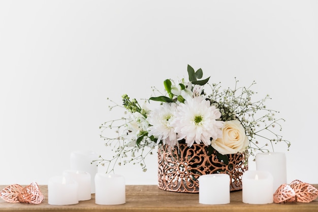 Free photo decorative flower vase with white candles on wooden table against white background