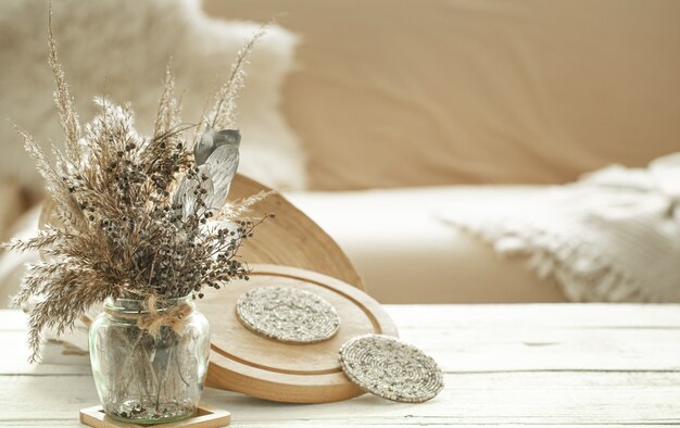 Decorative items in the cozy interior of the room, a vase with dried flowers on light wooden table.