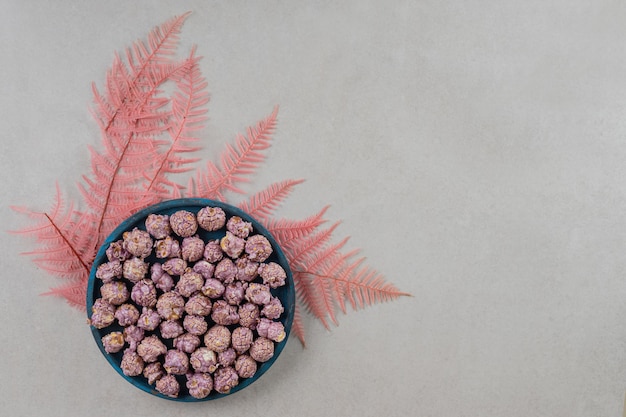 Free photo decorative leaves underneath a bowl of popcorn candy on marble background.