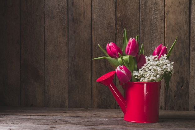 Free Photo decorative watering can with flowers on wooden table