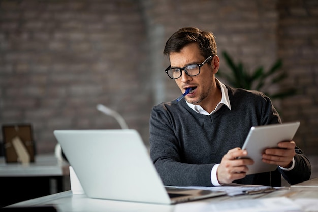 Free photo dedicated businessman using laptop and digital tablet while working in the office