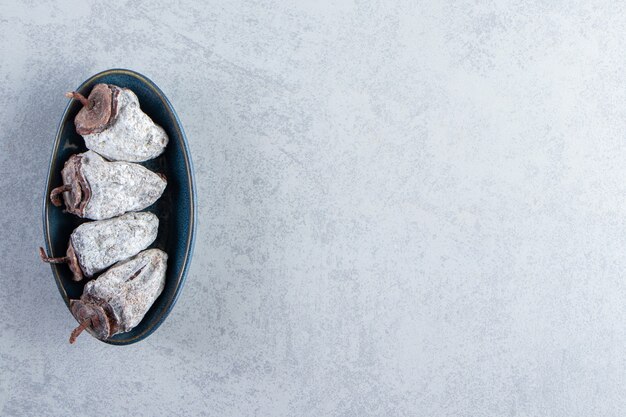 Deep blue plate of dried persimmon fruits on stone background.