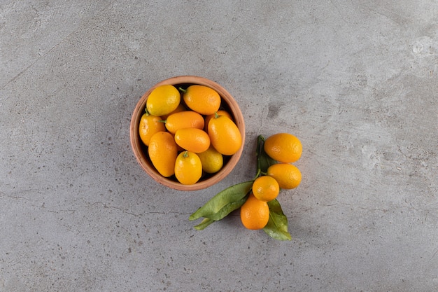 Deep bowl of fresh juicy kumquats on stone table.