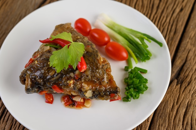 Free Photo deep-fried fish heads topped with chilies on a white plate with tomatoes and spring onions.