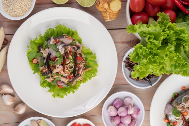 Deep-fried mackerel topped with galangal, pepper, mint, red onion in a white dish.