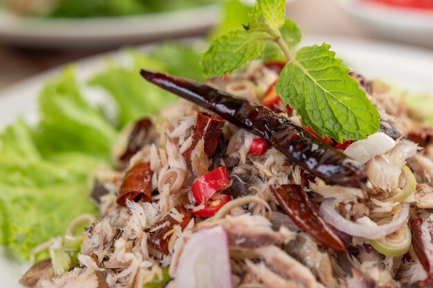 Deep-fried mackerel topped with galangal, pepper, mint, red onion in a white dish.