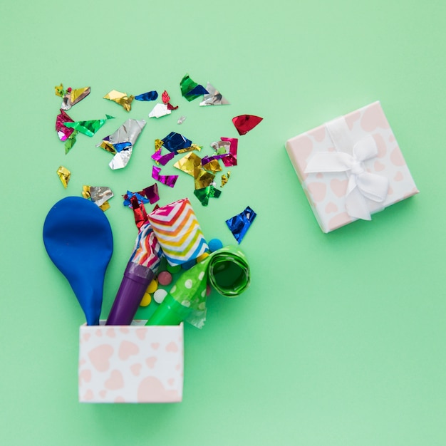 Free photo deflated balloon; party horn blowers and confetti in the open box on green background