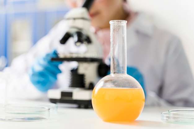 Defocused female scientist with microscope and lab glassware