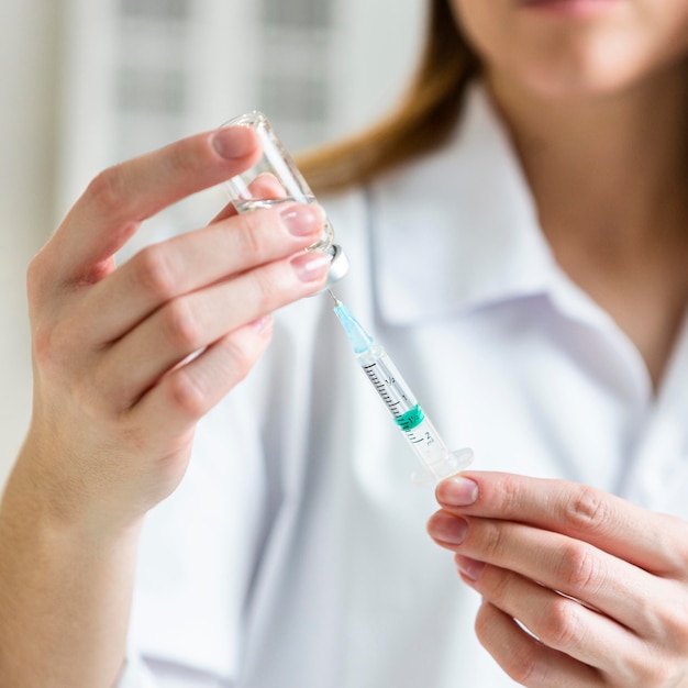 Defocused female scientist with safety glasses holding syringe with vaccine