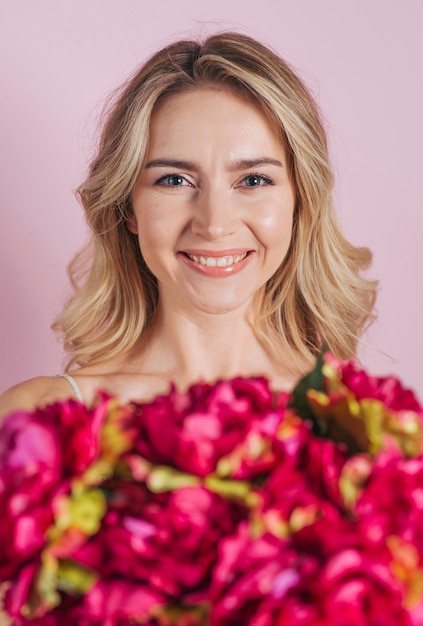 Free Photo defocused flower bouquet in front of smiling young woman against pink background